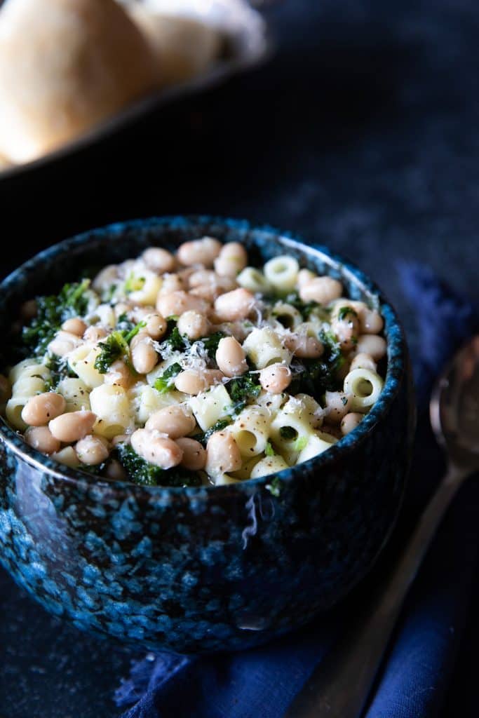 a bowl of white bean soup piled high with pasta and spinach