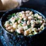 a close up of a bowl of white bean soup piled high with pasta and spinach