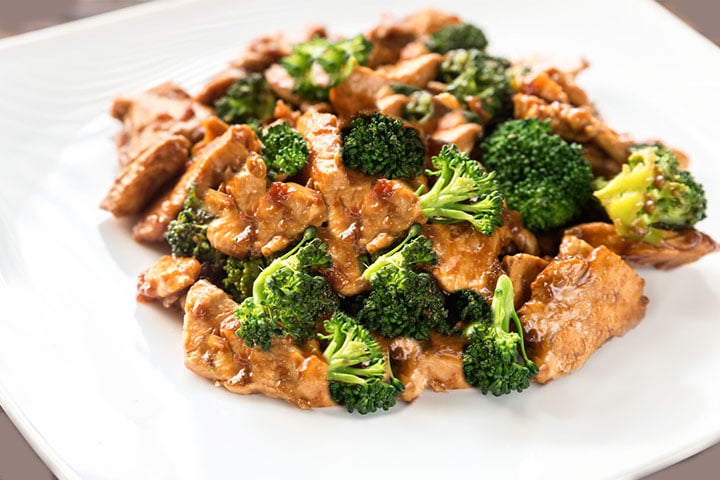 A close up of a white dish with the Chinese Chicken & Broccoli covered in a deep golden sauce.