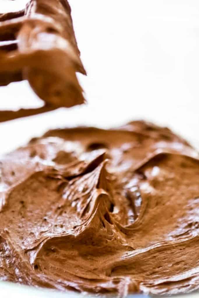 A bowl of freshly mixed chocolate frosting with beaters over the bowl