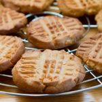 A cooling rack filled with fresh baked Classic Peanut Butter Cookies with golden edges and crisscross pattern
