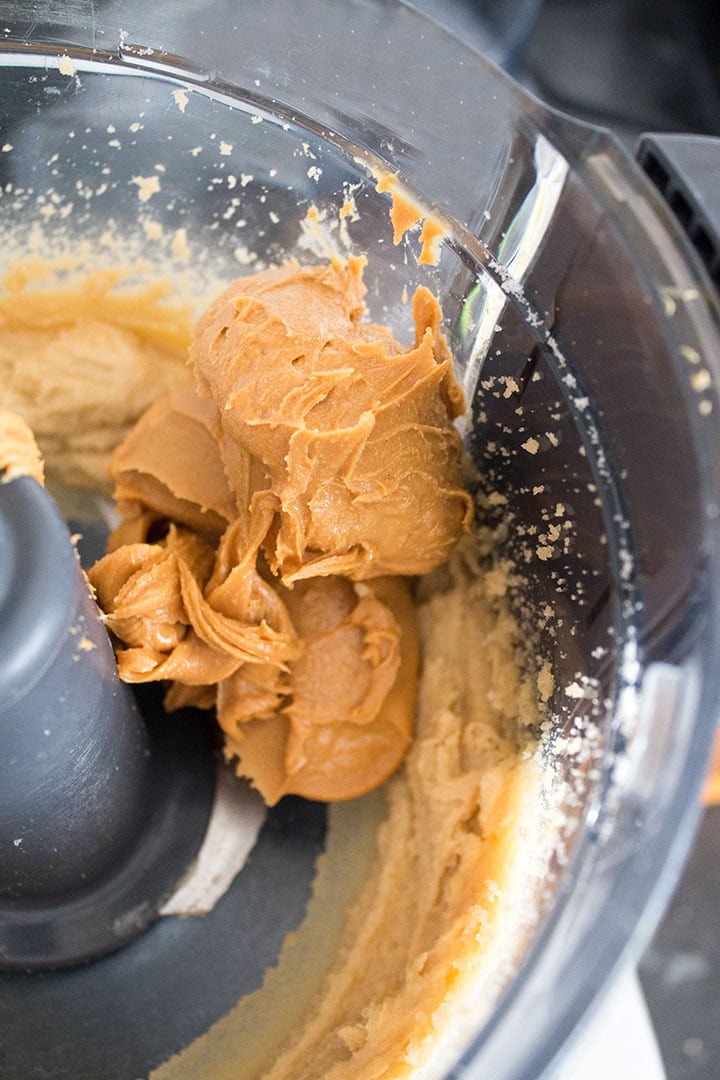 A close up of a food processor bowl with fluffy butter and sugar creamed together topped with a mound of peanut butter