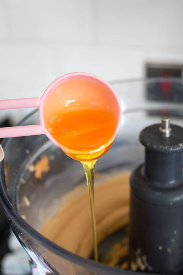 A measuring spoon pouring the golden syrup into the cookie dough mixture below.