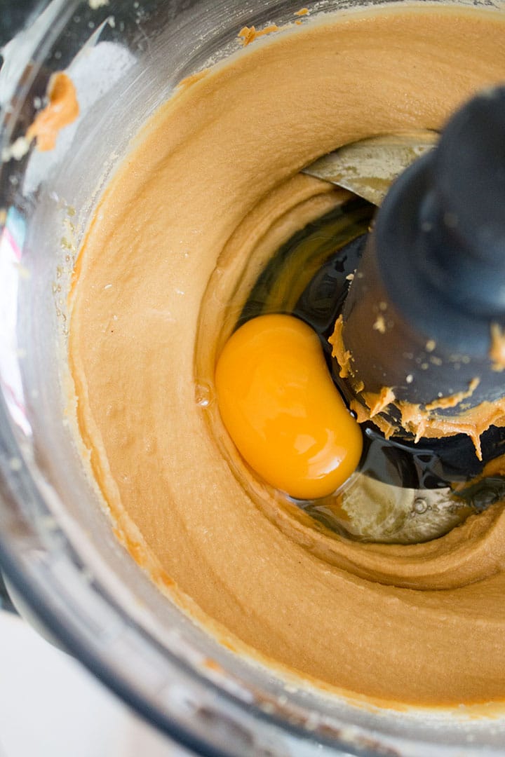 A food processor bowl mixed cookie dough and an egg on top ready to mix in