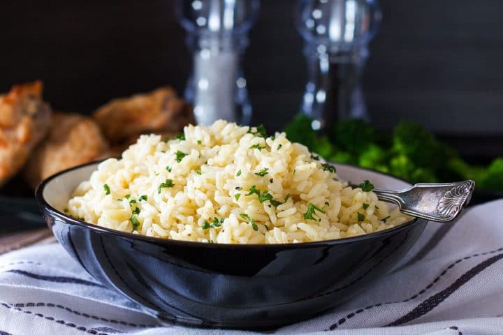 A serving bowl filled with Rice Pilaf sprinkled with chopped parsley.