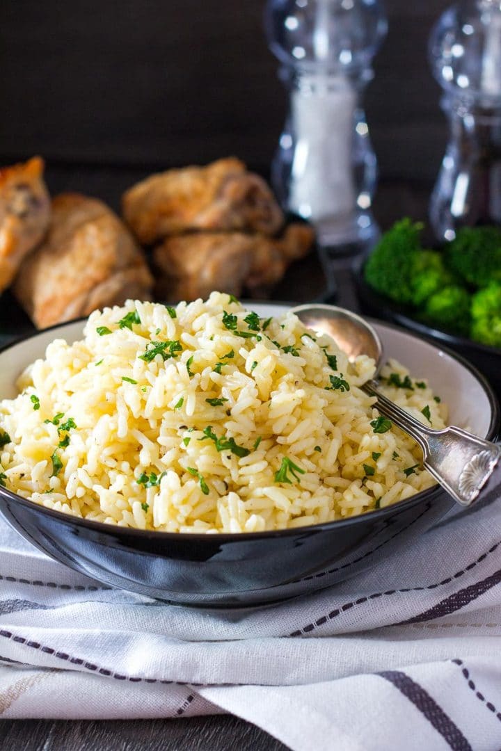 A bowl of Rice Pilaf with a platter of chicken and salt and pepper in the background.