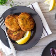 the crab cakes on a plate with lemon wedges and a dish of rice and a salad bowl in the background