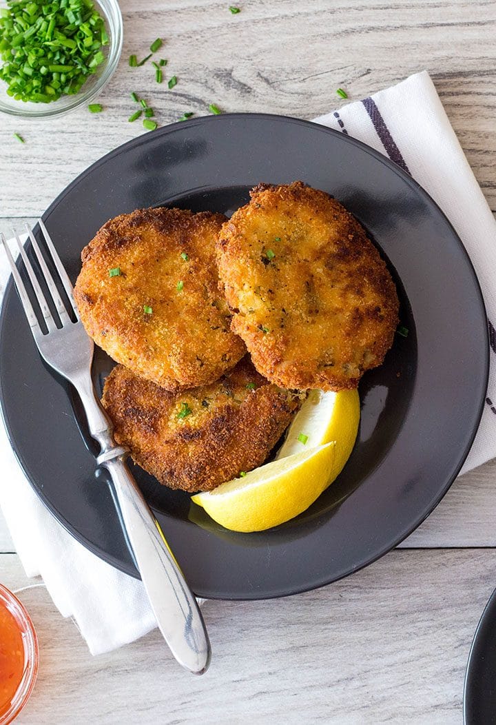 Three Crab Cakes on a plate with lemon wedges and a fork next to it