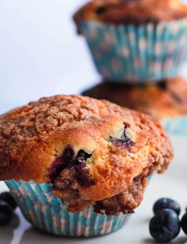 A Blueberry Crumb Cake Muffin on a plate with some fresh blueberries
