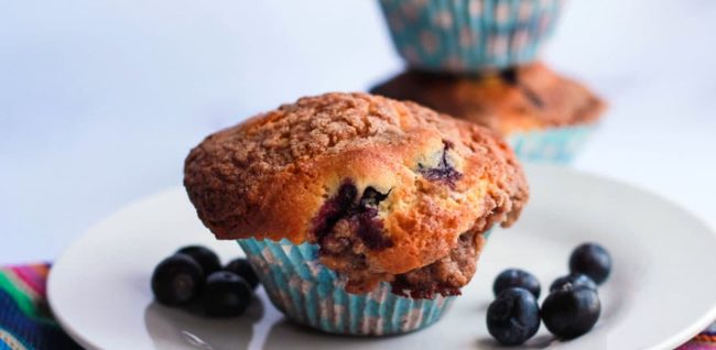 A blueberry muffin with a coffee cake crumb on the top.