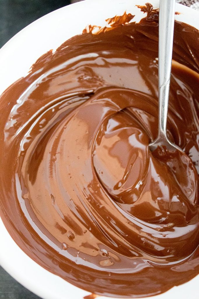 A bowl of melted chocolate with a spoon mixing it
