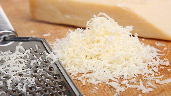 fresh grated Parmesan Cheese on a cutting board with a block of cheese next to it