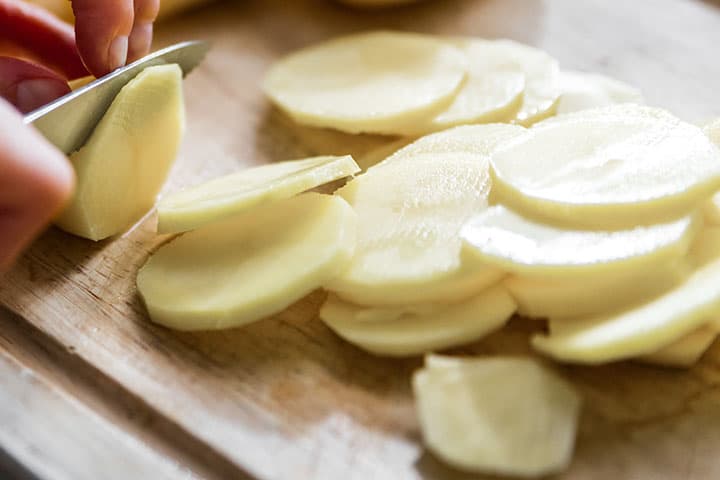 Potatoes being sliced on a cutting board