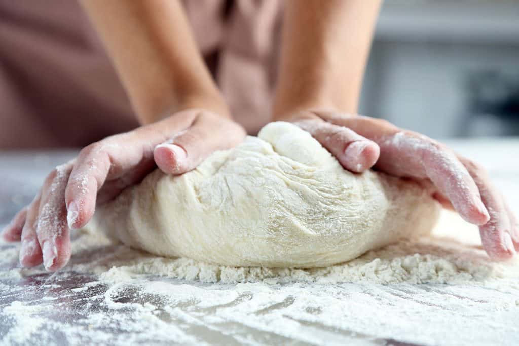 dough being kneaded by hand on a floured surface