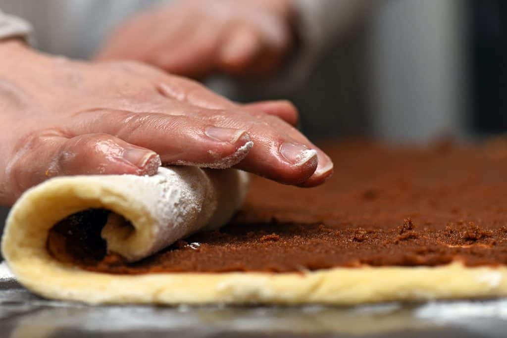 Cinnamon roll dough with filling being rolled up