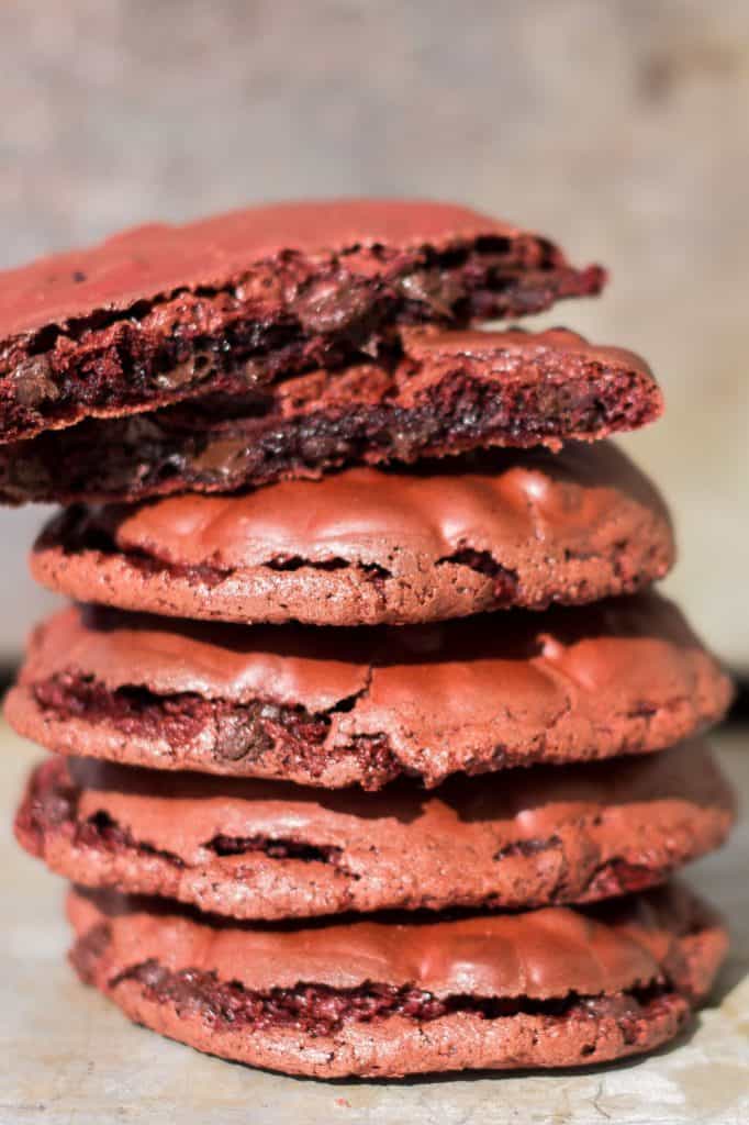A stack of red velvet cookies with the top one broken open to reveal the inside of the cookie
