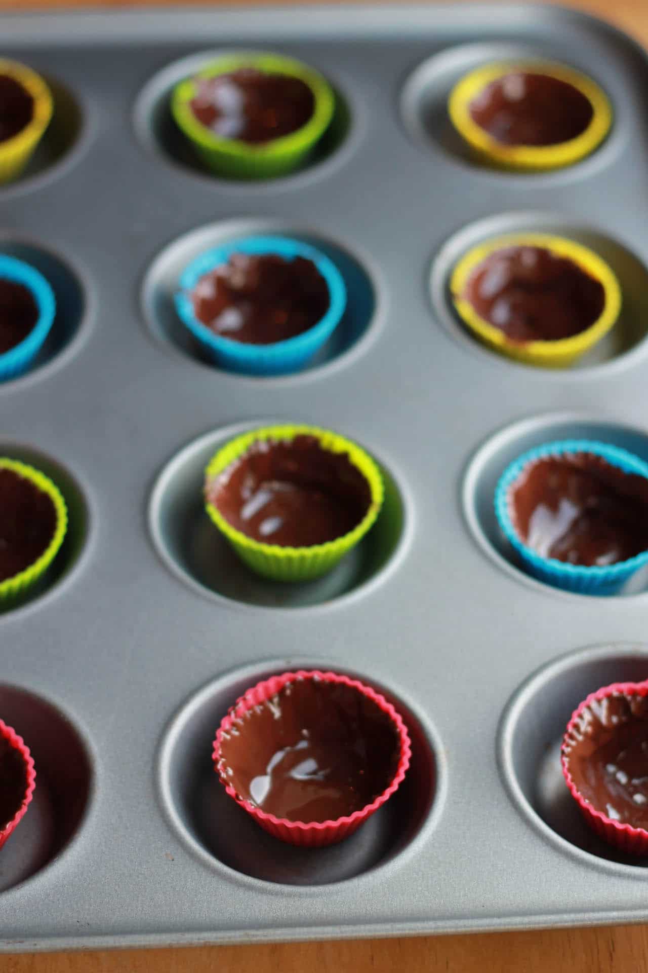 silicone cup cake cases in a cake pan with melted chocolate inside.