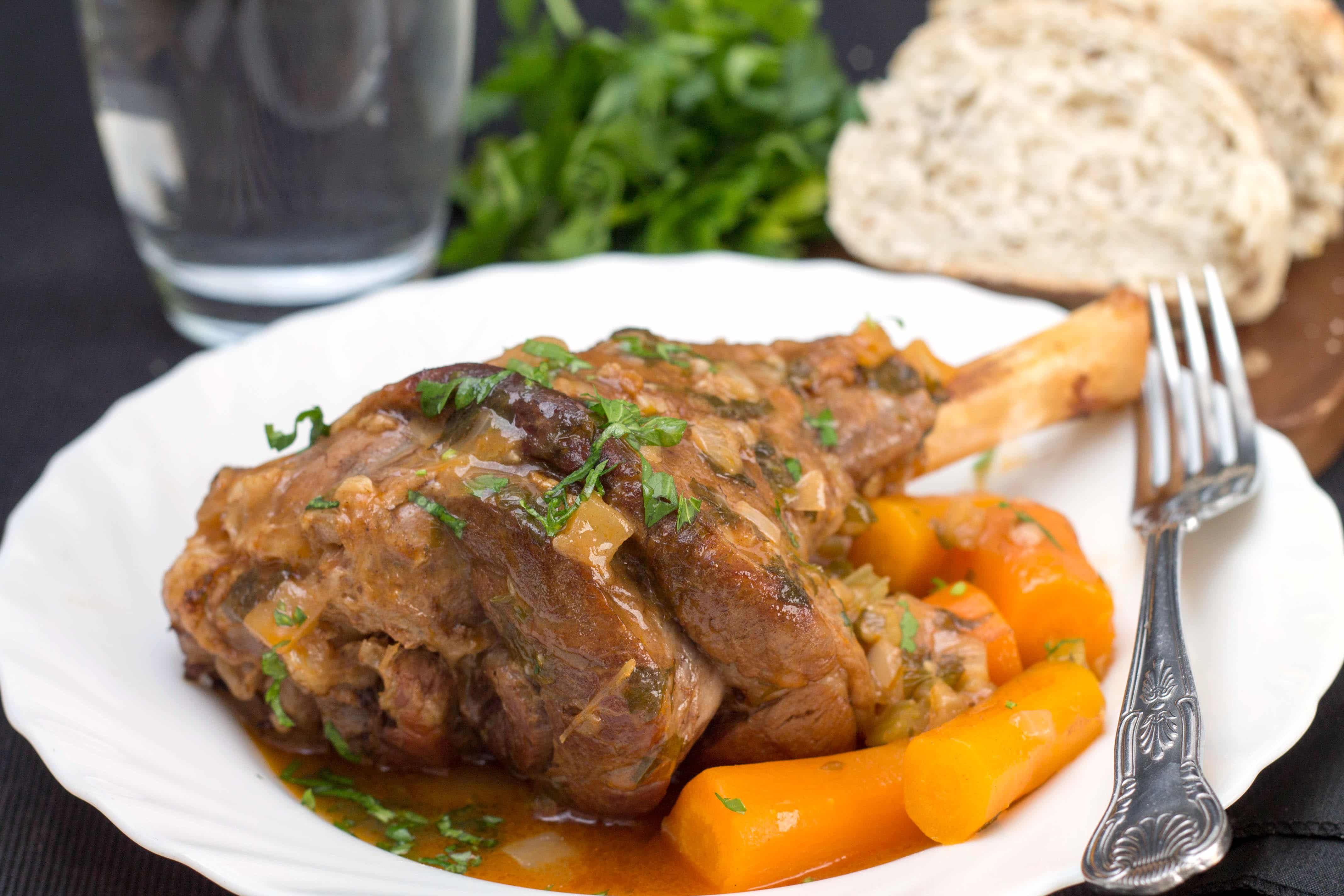 Slow cooked lamb shanks in a dish with accompanying vegetables.