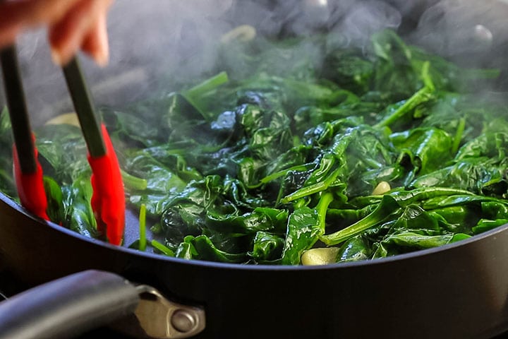 Spinach in a pan being stirred with tongs