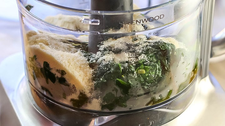 The spinach and garlic added to a food processor with grated cheese and pasta water