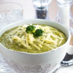 a Bowl full of Healthy creamy broccoli soup with shredded cheese and broccoli on top
