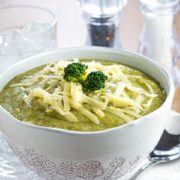 a Bowl full of Healthy creamy broccoli soup with shredded cheese and broccoli on top