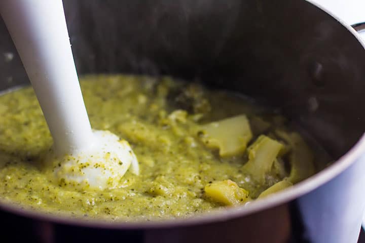 The Healthy creamy broccoli soup being blended with a stick blender