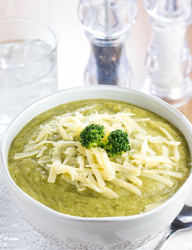 a Bowl full of Healthy creamy broccoli soup with shredded cheese and broccoli on top