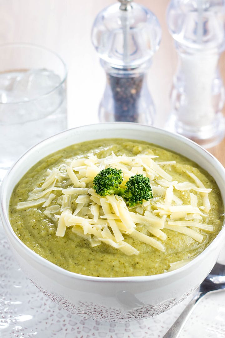 a Bowl full of Healthy creamy broccoli soup with shredded cheese and broccoli on top