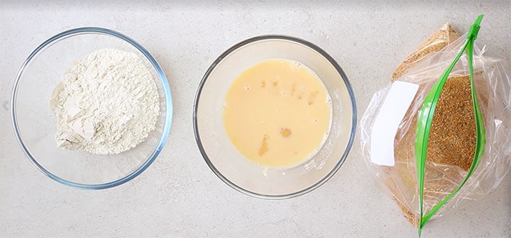 The egg, and flour in glass bowls next to the breadcrumbs in a plastic bag.