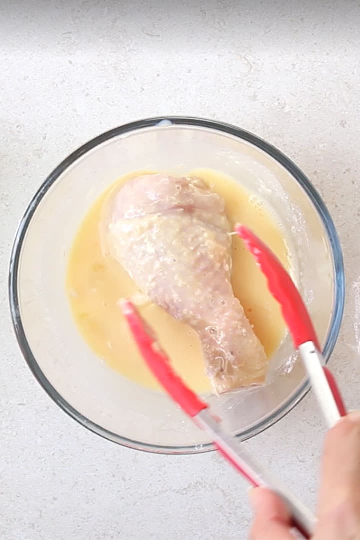 The flour coated chicken being dipped in the egg mixture