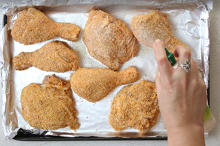 A pan of chicken pieces coated with breadcrumbs being spayed with cooking spray.