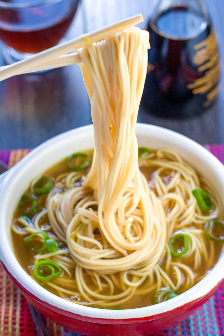 A bowl of quick and easy Chinese noodle soup with chopsticks holding some noodles above the bowl