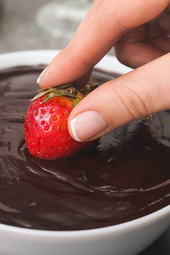 a strawberry being dipped into a bowl of chocolate
