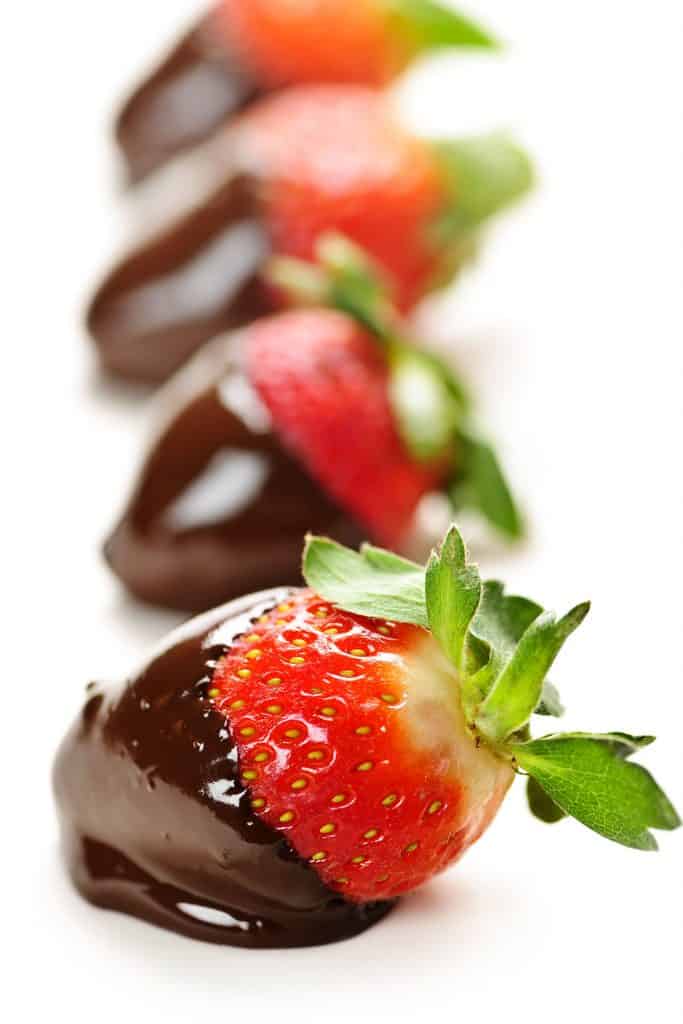Freshly dipped chocolate covered strawberries on a sheet of parchment paper
