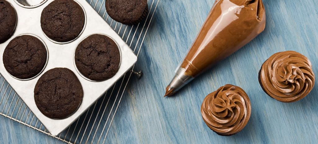 a piping bag filled with chcolate frosting next to frosted and unfrosted cupcakes