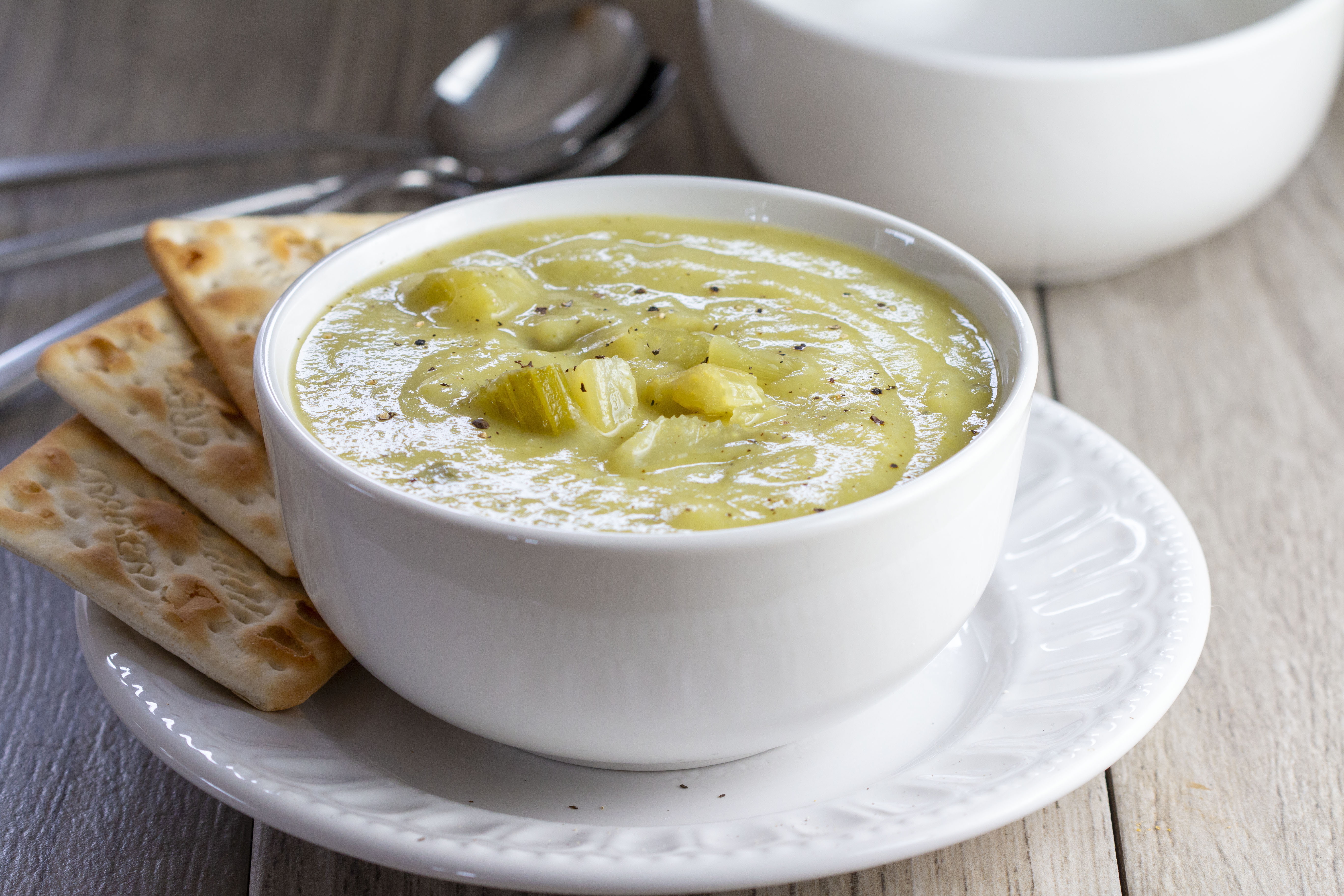 A bowl of Creamy Celery Soup with crackers on the side of the bowl