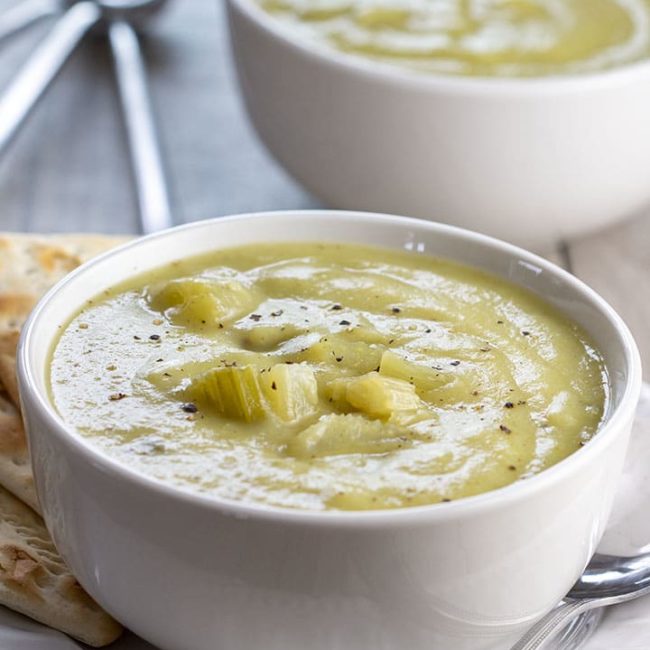 Two bowls of Creamy Celery Soup with crackers on the side of the bowl