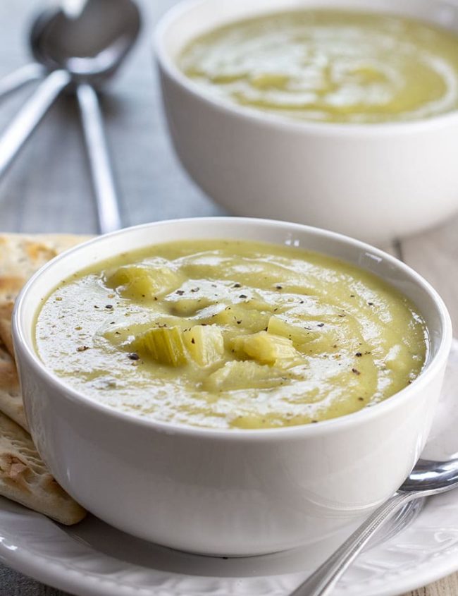 Two bowls of Creamy Celery Soup with crackers on the side of the bowl