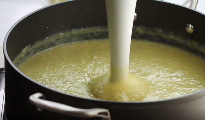 A close up of the celery soup being pureed with a stick blender