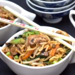 A bowl of food on a plate, with Noodles and chopsticks