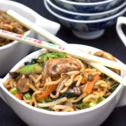 A bowl of food on a plate, with Noodles and chopsticks