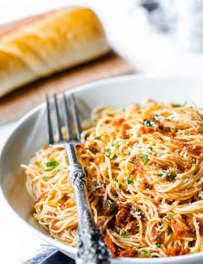 A plate of angel hair pasta with pesto sauce sprinkled with grated cheese and chopped parsley
