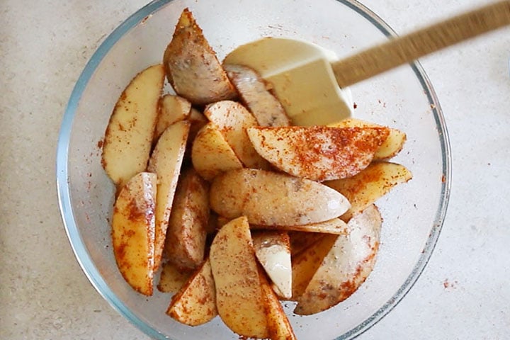 The wedges in a bowl coated with seasoning.