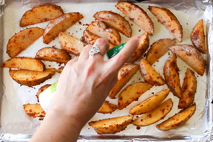 the wedges on a baking tray being sprayed with cooking spray
