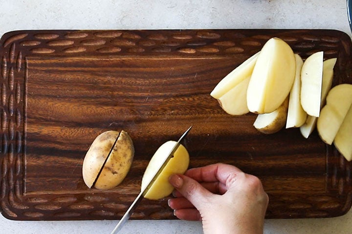 The raw potatoes on a cutting board being cut into wedges