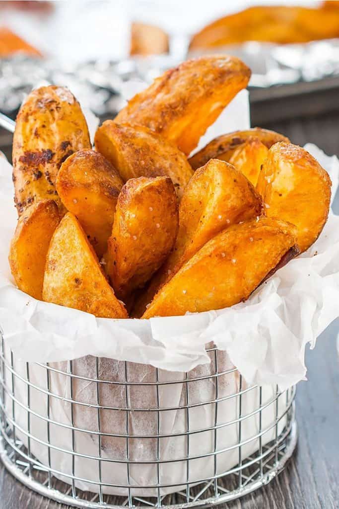 Seasoned Baked Potato Wedges in a metal serving basket sprinkled with salt.