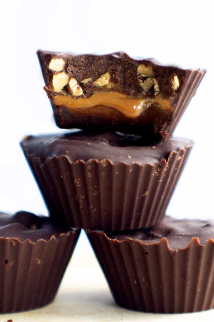 4 homemade snickers cups candies with one cut open to see the caramel and peanuts inside