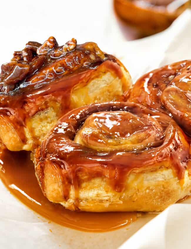 A close-up view of freshly baked sticky buns with a glossy, caramelized topping that's dripping with rich, golden-brown caramel sauce.
