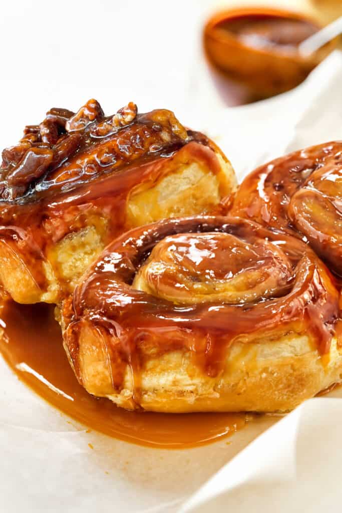 A close-up view of freshly baked sticky buns with a glossy, caramelized topping that's dripping with rich, golden-brown caramel sauce.